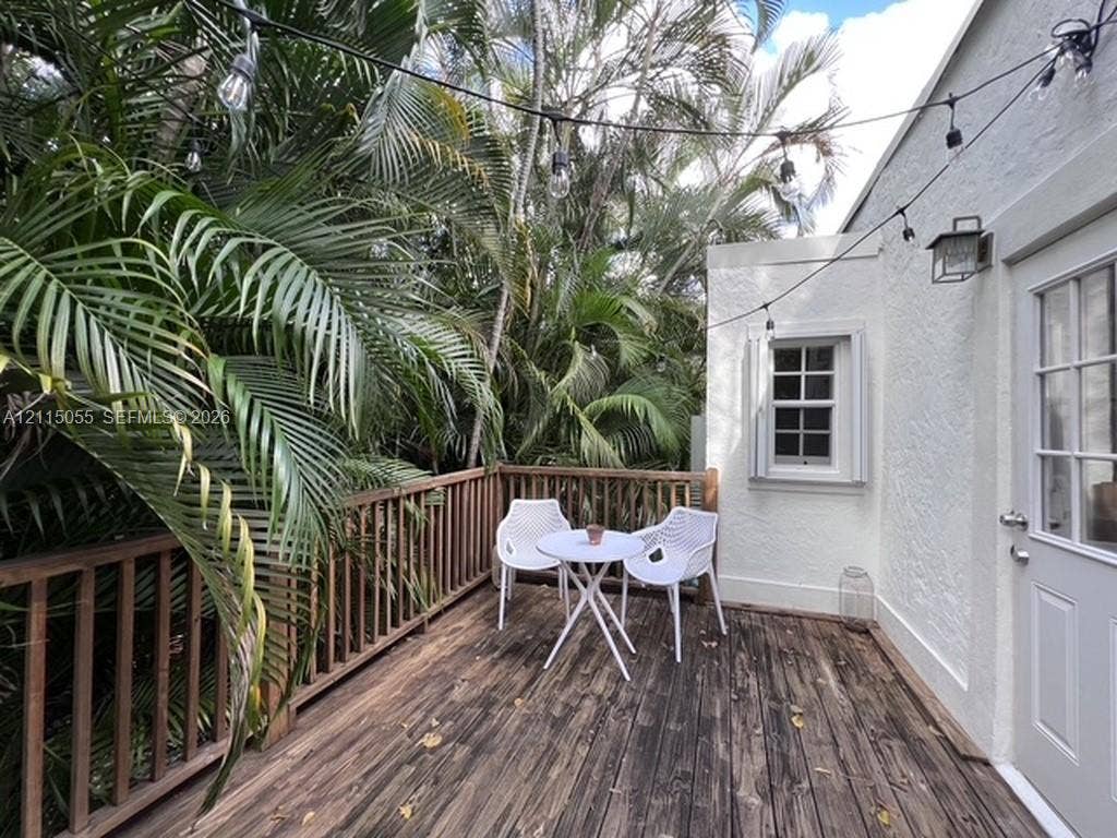11728 NE 6th Avenue, #2, Biscayne Park, Biscayne Park, FL 33161 Exterior wood deck featuring a balustrade railing, white textured stucco siding, multi-pane window, and attached wall-mounted lantern light