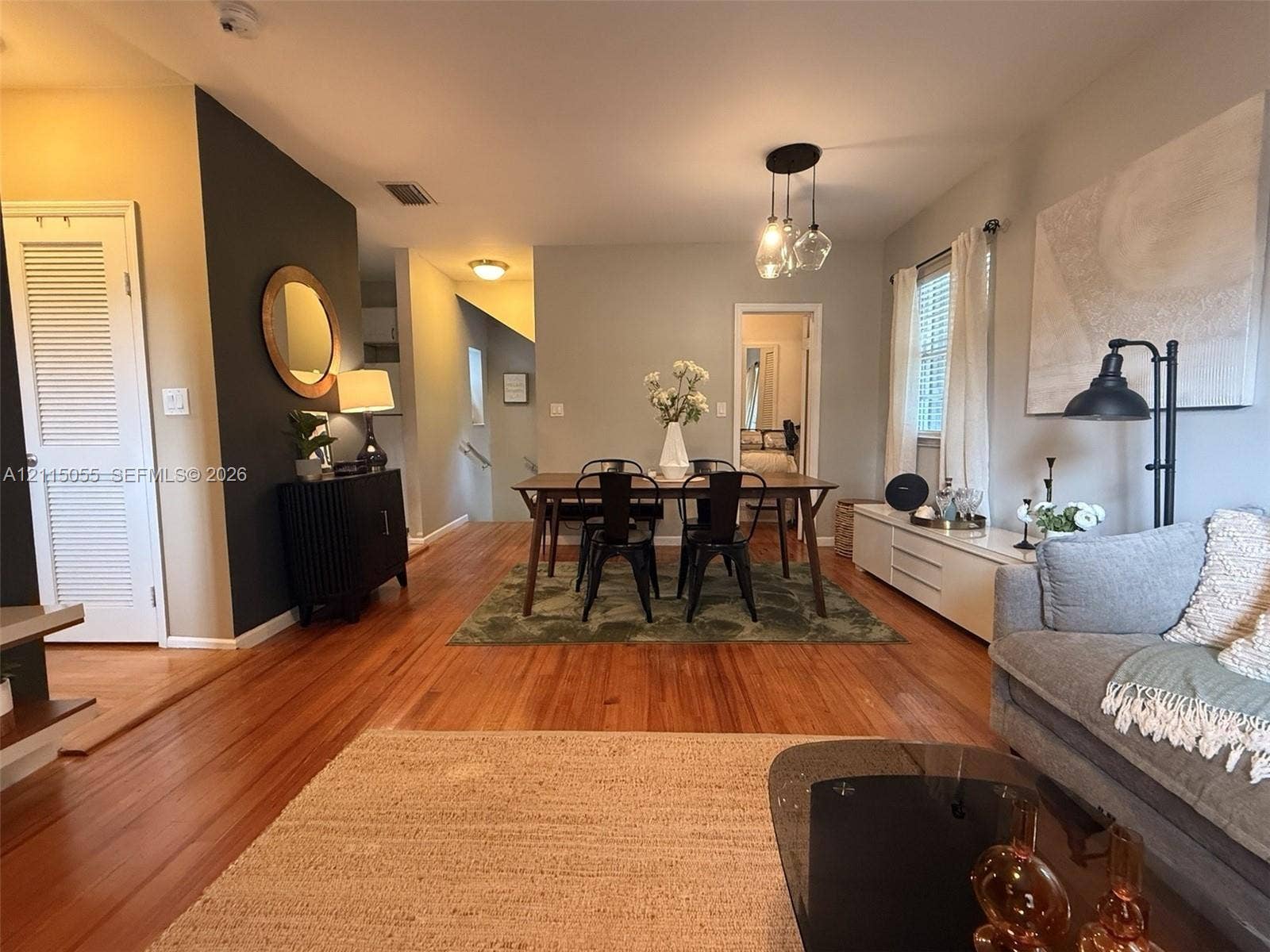 11728 NE 6th Avenue, #2, Biscayne Park, Biscayne Park, FL 33161 Open-concept living and dining area featuring wood-finish flooring, a dark charcoal accent wall, multi-pendant lighting, and louvered closet doors