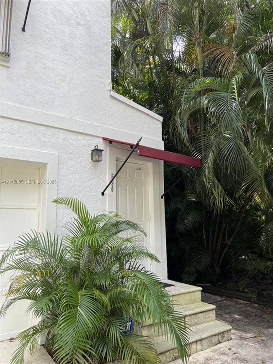 11728 NE 6th Avenue, #2, Biscayne Park, Biscayne Park, FL 33161 Stucco exterior featuring a six-panel entry door, metal awning, stone-finish steps, and a wall-mounted lantern fixture