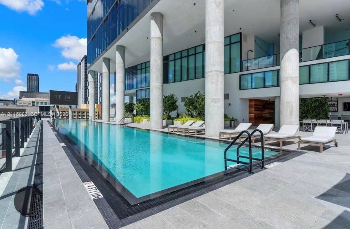 Swimming pool with concrete deck, structural pillars, and glass-paneled building exterior