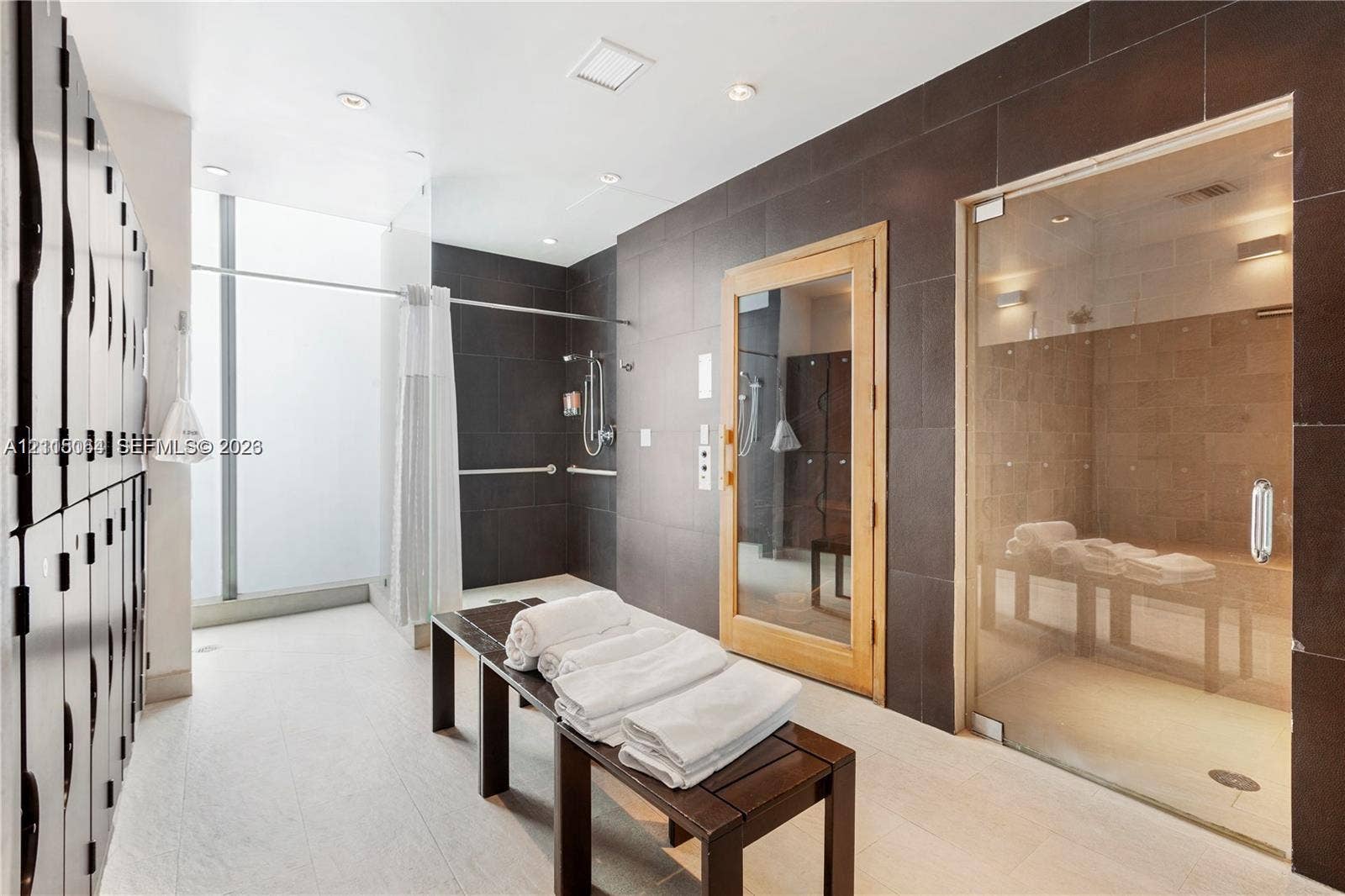 17315 Collins Avenue, #1808, Sunny Isles Beach, FL 33160 Spa area featuring a glass-enclosed steam room, a sauna with wood-framed glass door, floor-to-ceiling dark tile wall accents, built-in locker storage, and a shower area with wall-mounted plumbing fixtures
