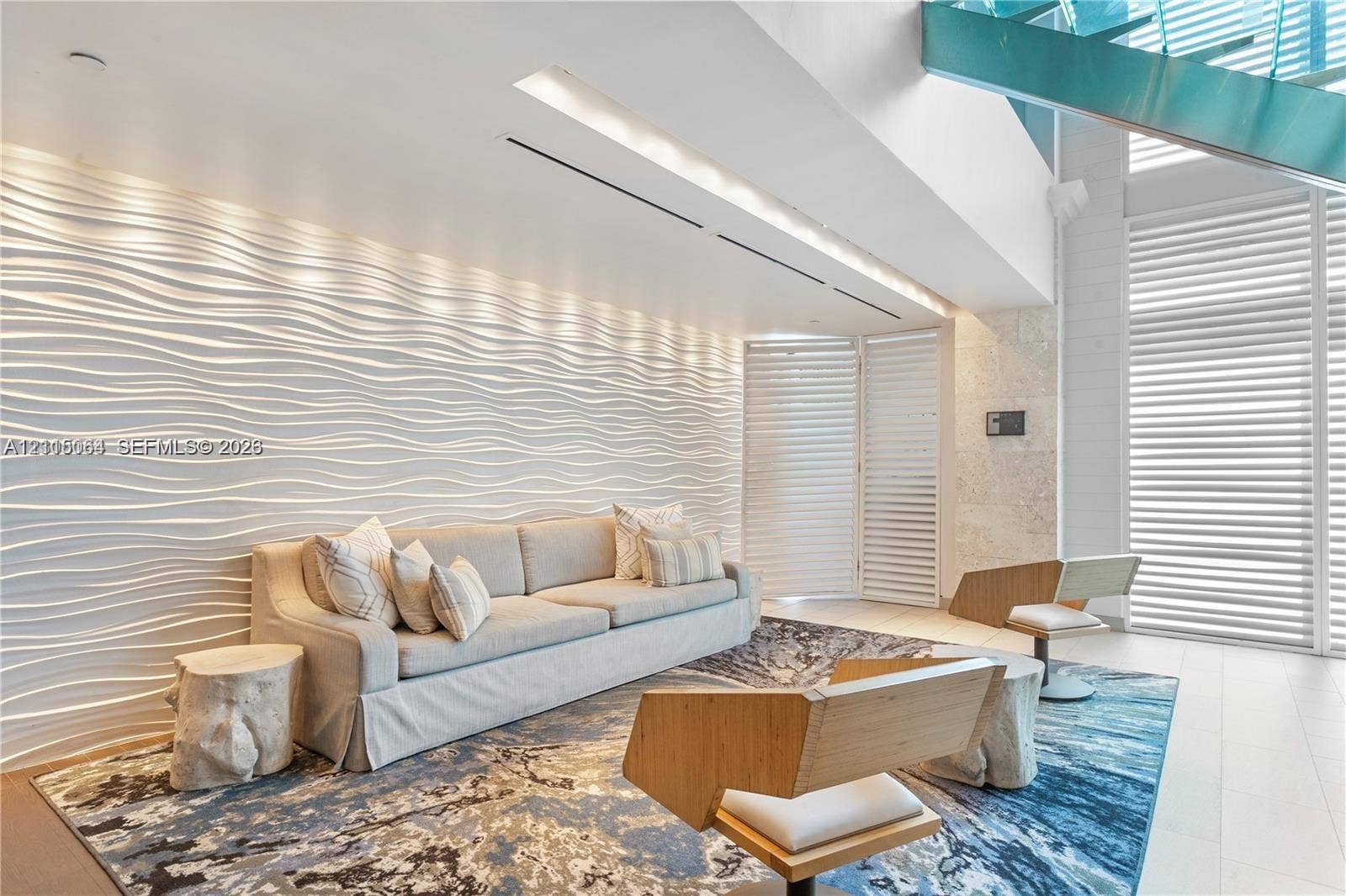 17315 Collins Avenue, #1808, Sunny Isles Beach, FL 33160 Textured wave-pattern accent wall, double-height ceilings, floor-to-ceiling louvered window treatments, glass-paneled staircase, and light-toned stone-finish flooring