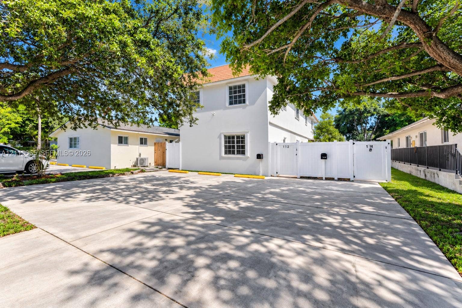 Concrete parking area featuring marked spaces, exterior white stucco siding, and white vinyl privacy fencing