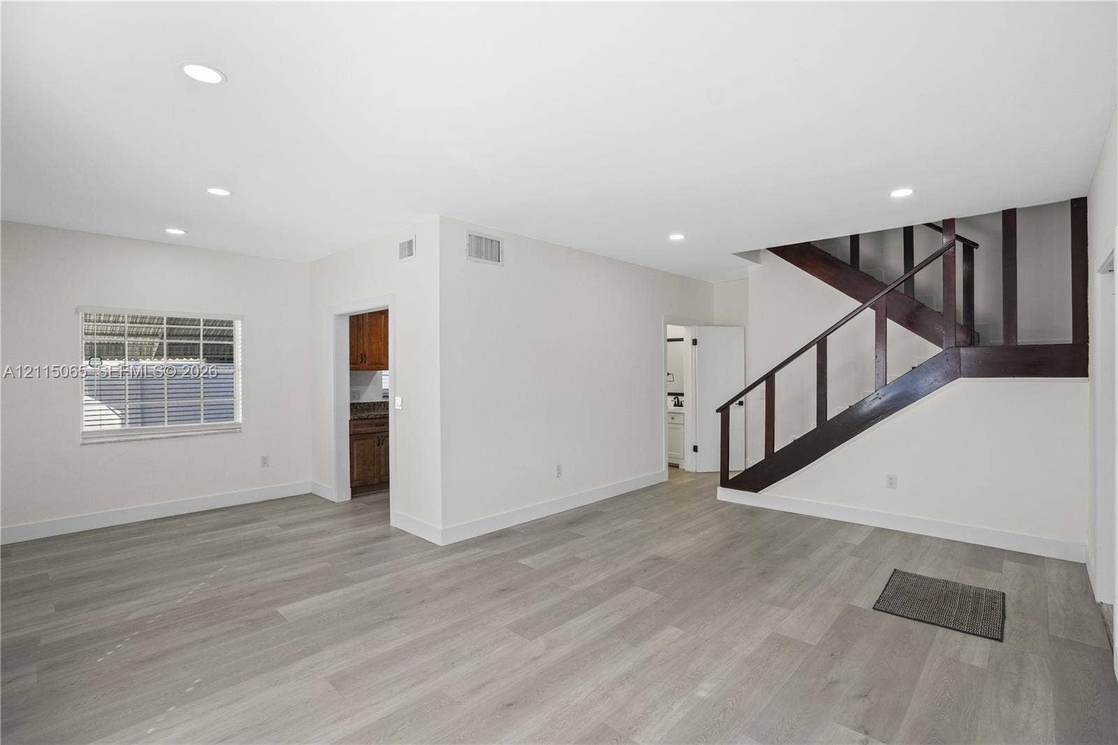 Open floor plan featuring light wood-finish flooring, recessed lighting, and a staircase with stained wood railings
