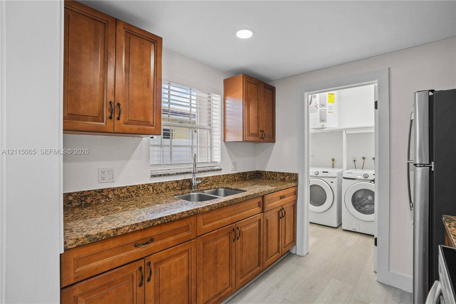 Kitchen featuring stained wood cabinetry, stone-surface countertops, dual-basin stainless steel sink with high-arch faucet, recessed ceiling lighting, and hard-surface flooring