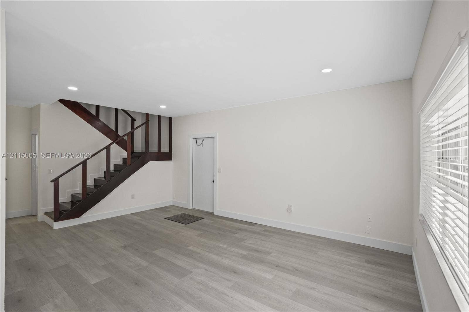 Open interior space featuring wood-finish flooring, recessed lighting, and a staircase with dark-toned railings and vertical slats