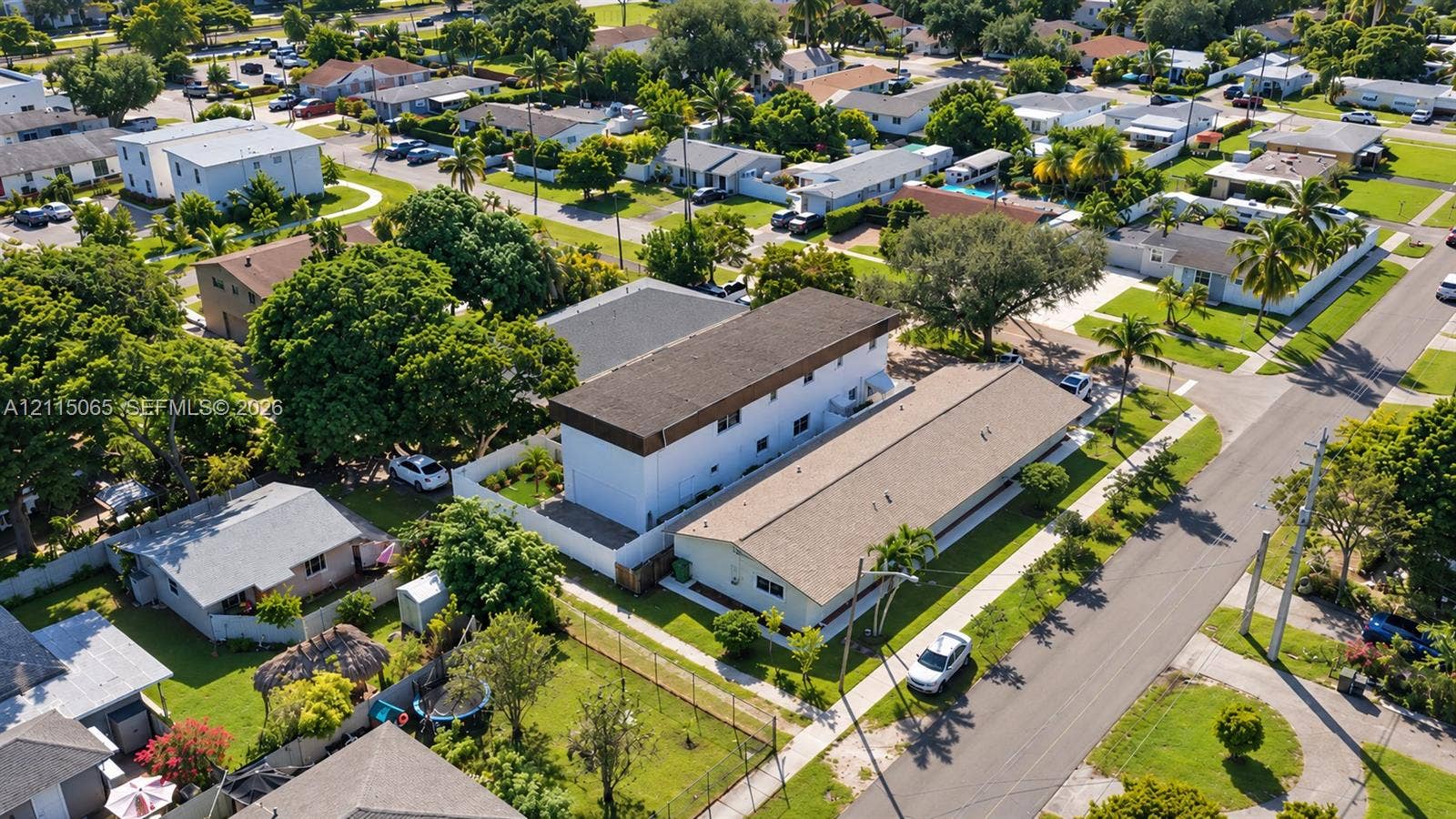 Aerial perspective of a multi-level structure featuring a flat roofline, white exterior siding, and a fenced perimeter