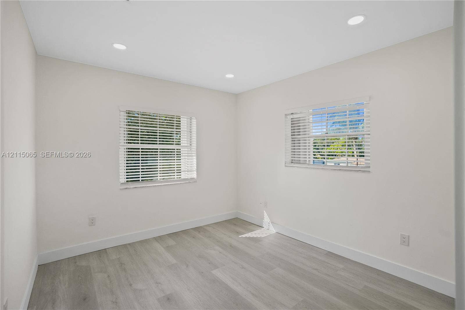 Neutral-toned interior featuring wood-finish flooring, recessed lighting, and dual windows with horizontal blinds