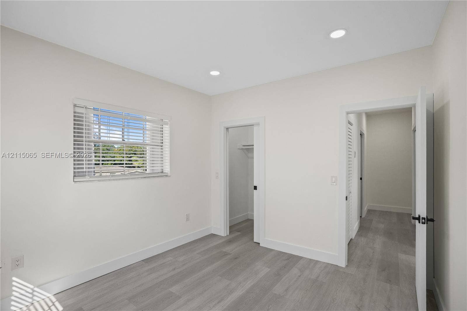 Neutral-toned interior featuring wood-finish flooring, recessed lighting, a horizontal window with blinds, and built-in closet storage