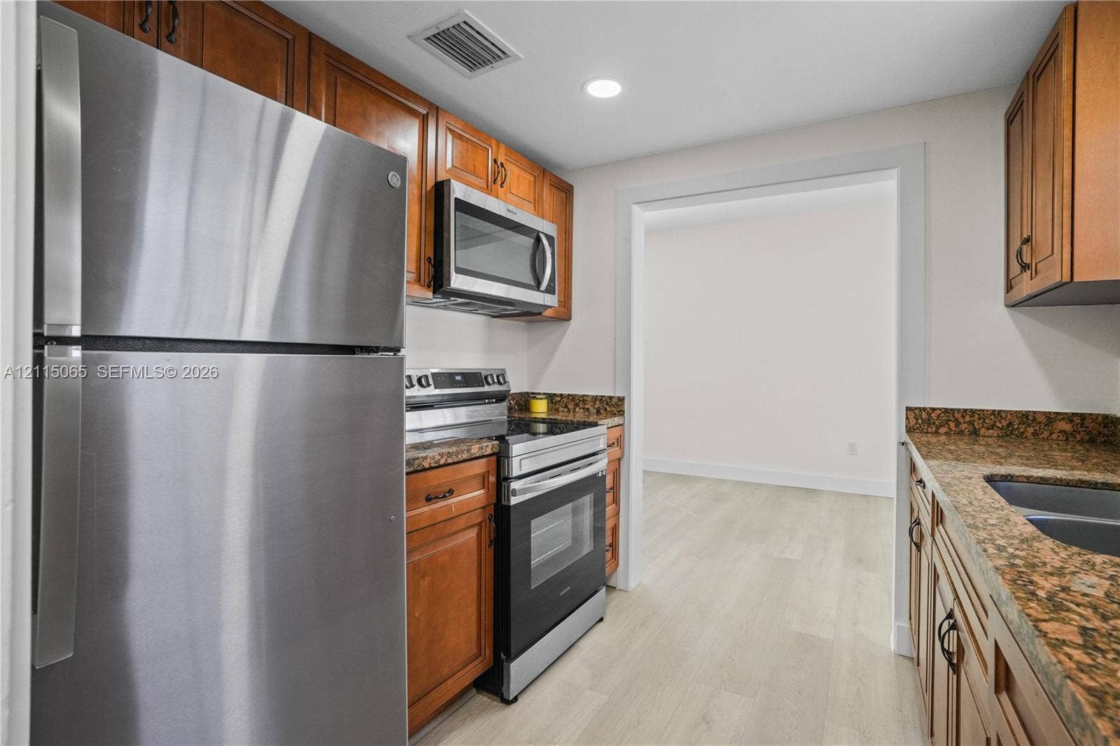 Kitchen featuring wood cabinetry, stone countertops, stainless steel appliances, and light-tone wood-finish flooring