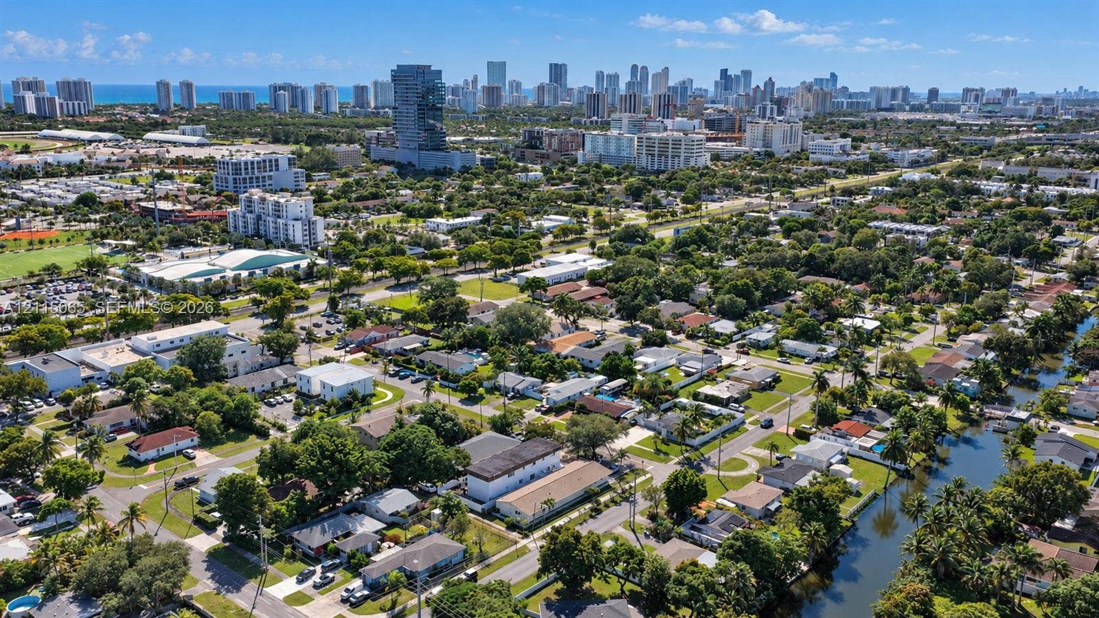 Aerial perspective of residential area featuring a waterway, mature tree canopy, and proximity to the coastal urban skyline