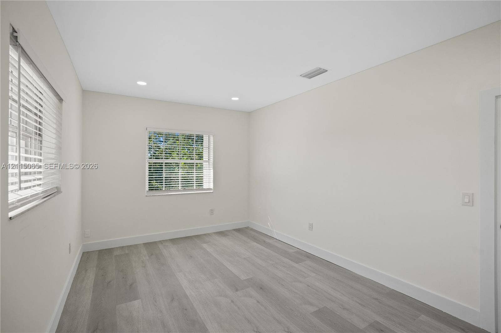 Neutral-toned interior room featuring wood-finish flooring, recessed lighting, and multiple windows with horizontal blinds