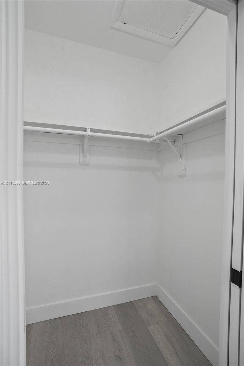 Storage space featuring wood-finish flooring and L-shaped shelving with integrated hanging rods