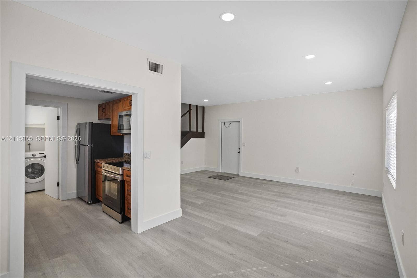 Open interior space featuring light wood-finish flooring, recessed lighting, and a kitchen equipped with stainless steel appliances, dark wood-tone cabinetry, and stone-surface countertops