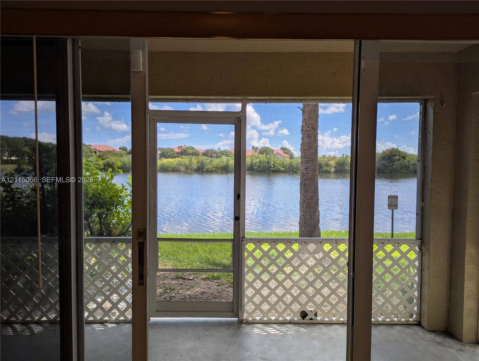 215 SW 120th Avenue, #215, Pembroke Pines, Pembroke Pines, FL 33025 Screened-in patio featuring a concrete floor, white lattice wall panels, and a swinging screen door, oriented toward a pond