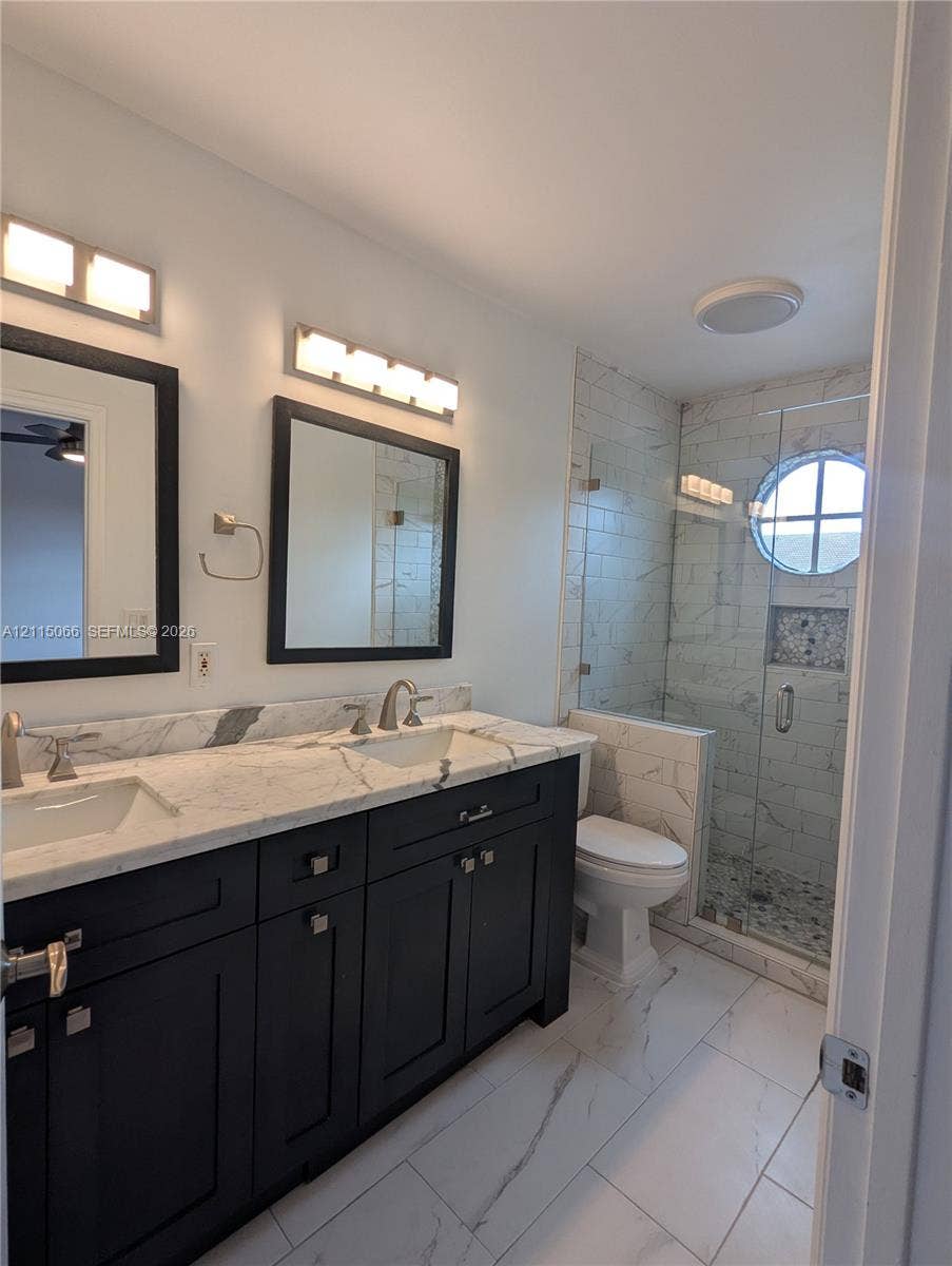 215 SW 120th Avenue, #215, Pembroke Pines, Pembroke Pines, FL 33025 Double vanity with stone countertop and dual undermount sinks, custom dark cabinetry, large-format tile flooring, and walk-in glass-enclosed shower featuring a porthole window and decorative tile inlay