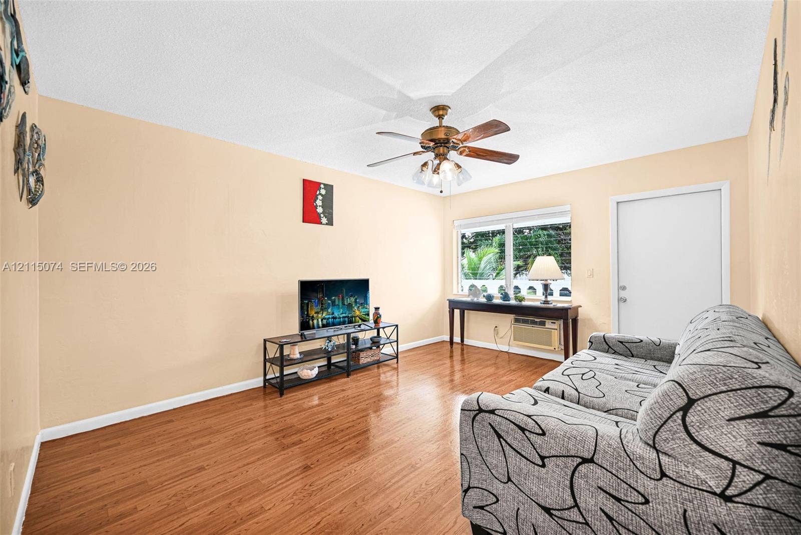 Room featuring wood-finish flooring, a multi-blade ceiling fan with integrated lighting, and a window with white trim