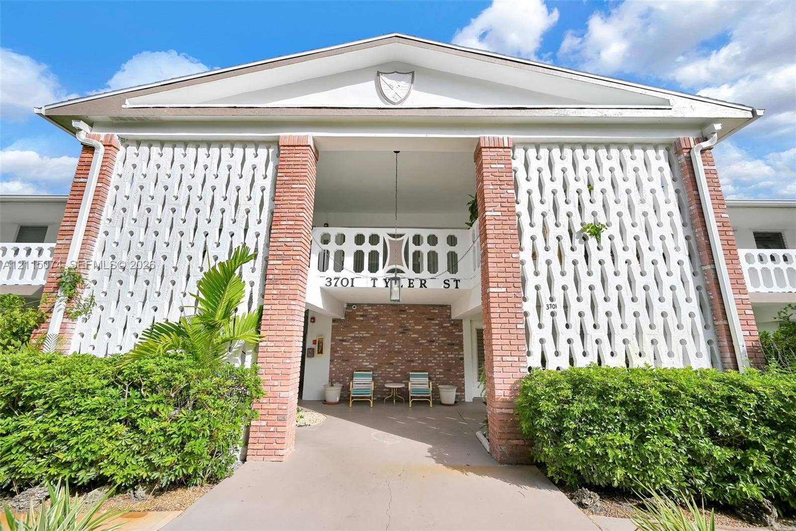 Exterior facade featuring a prominent brick-trimmed entrance, patterned concrete screen walls, a decorative gable pediment, and a second-level balcony with intricate railings