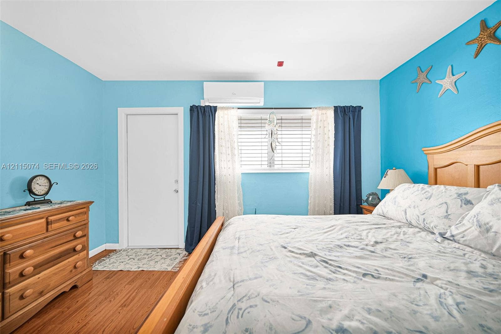 Wood-finish flooring, wall-mounted ductless air conditioning unit, and white window blinds