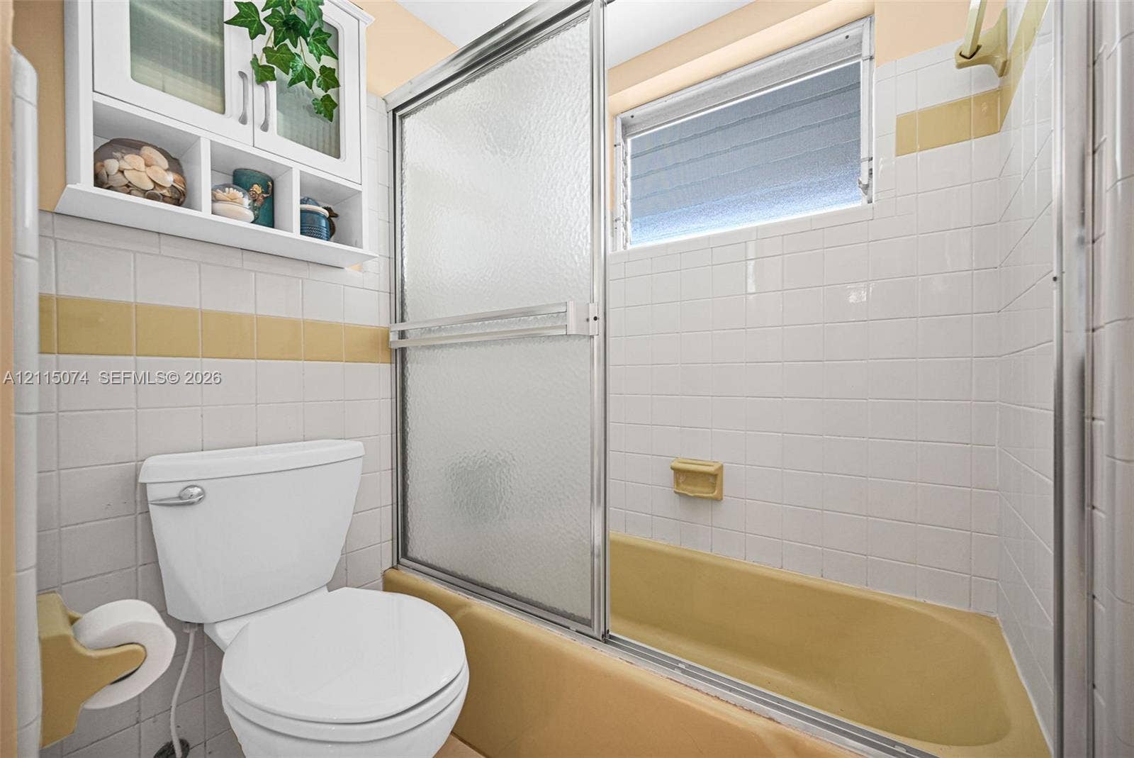 Bathroom featuring white wall tiling with accent banding, a porcelain tub, sliding glass shower doors, and white built-in wall cabinetry