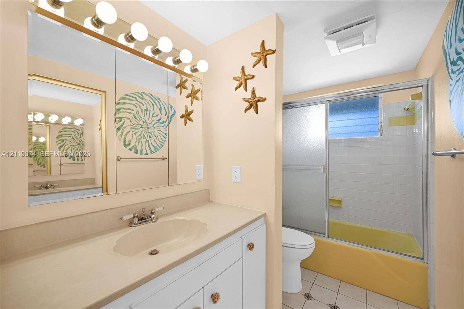 Bathroom featuring a white vanity cabinet with an integrated sink, a large wall-to-wall mirror, multi-bulb overhead lighting, and a tub-shower combination with a sliding glass door