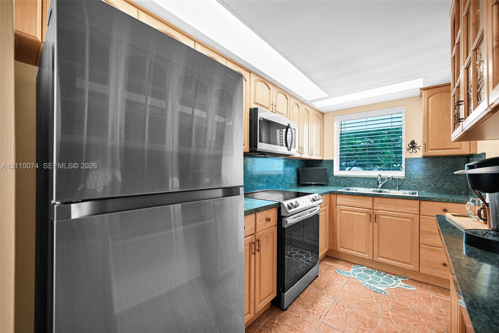 Kitchen featuring light wood cabinetry, stone-finish countertops, stainless steel appliances, a double-basin sink, and tile flooring