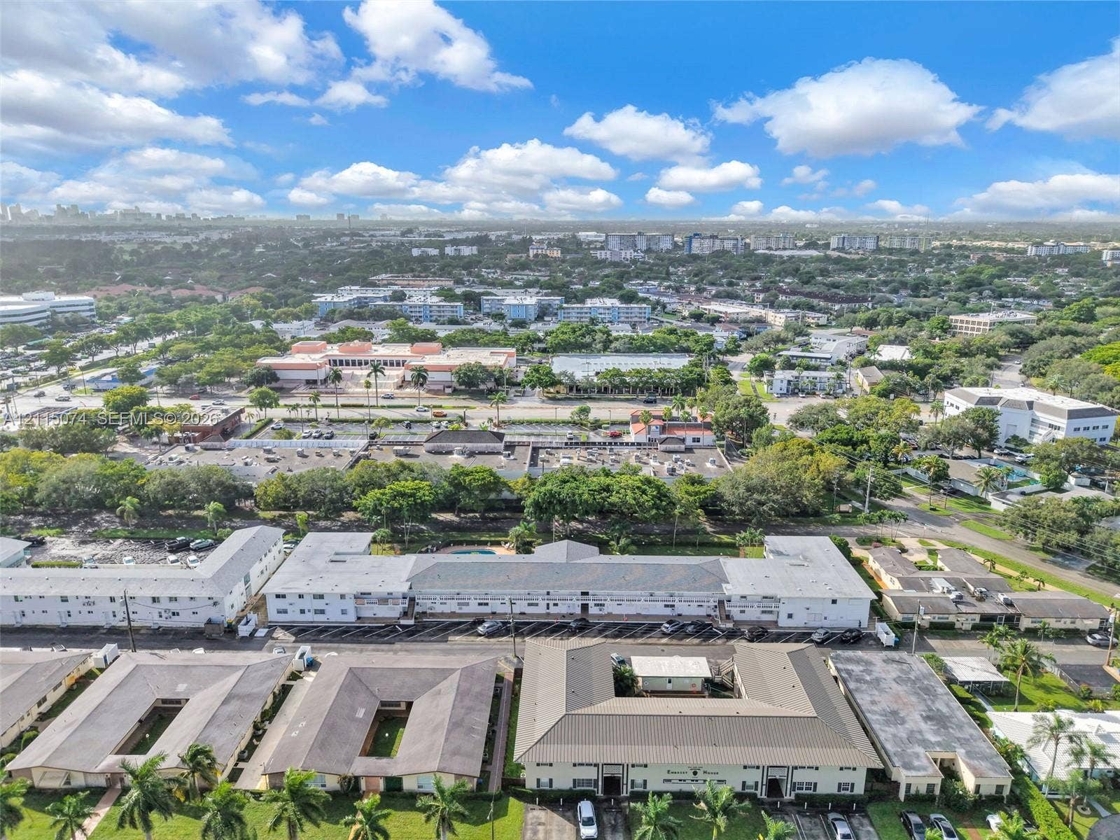 Aerial perspective showcasing a multi-unit residential complex featuring a central courtyard, paved surface parking, low-pitch rooflines, and exterior landscaping with palm trees