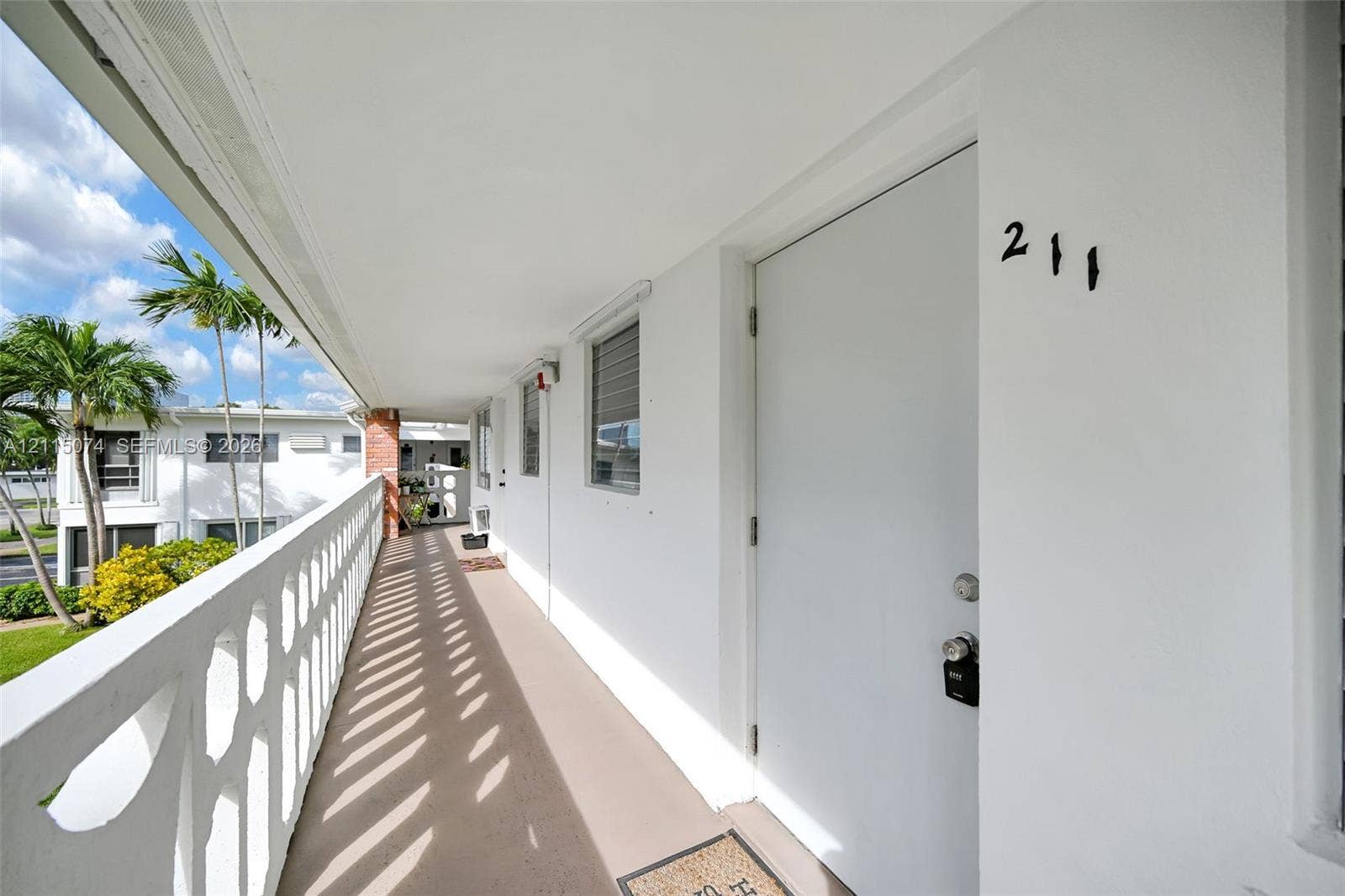 Covered exterior walkway featuring a decorative concrete balustrade and solid-core entry door