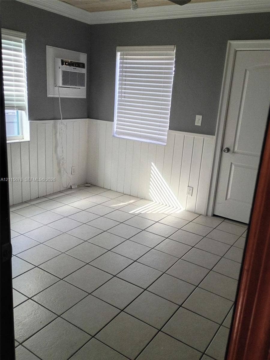 209 SW 12th Street, #A, Dania, Dania Beach, FL 33004 Interior space featuring square tile flooring, white vertical wainscoting, two windows with horizontal blinds, and a paneled interior door