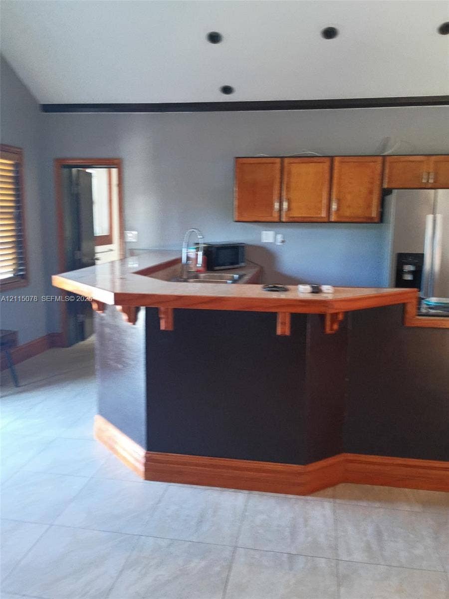 209 SW 12th Street, #A, Dania, Dania Beach, FL 33004 Kitchen featuring a tiered wood-topped breakfast bar, recessed ceiling lighting, wood-finish upper cabinetry, and light-toned tile flooring