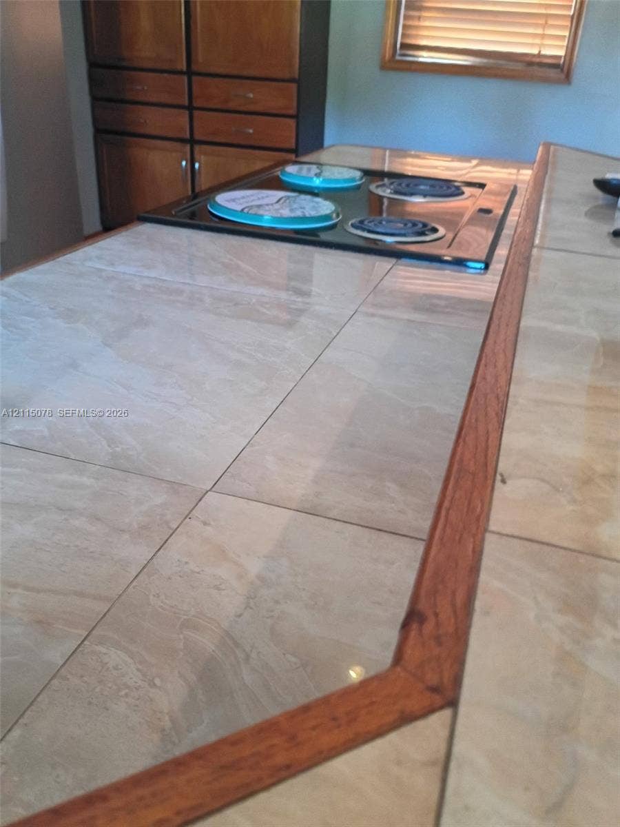 209 SW 12th Street, #A, Dania, Dania Beach, FL 33004 Tiled kitchen countertop with wood trim, integrated electric cooktop, and built-in cabinetry