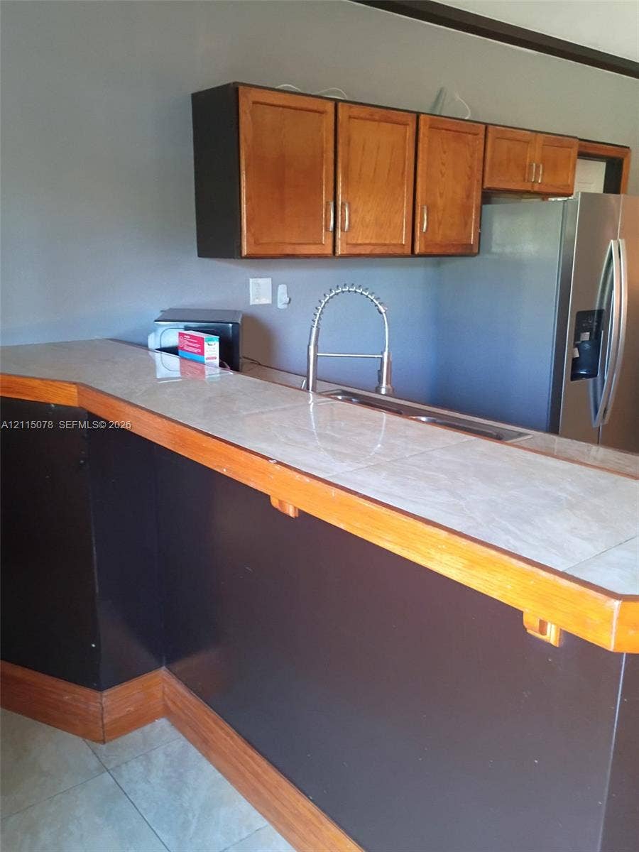 209 SW 12th Street, #A, Dania, Dania Beach, FL 33004 Kitchen peninsula featuring tiled countertop, wood-trim edge, stainless steel sink with high-arc pull-down faucet, and upper wood cabinetry