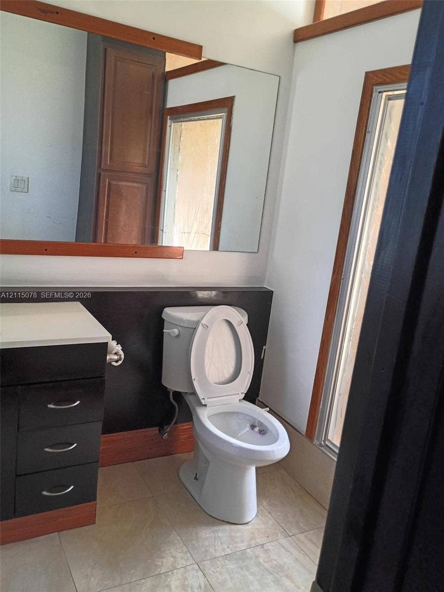 209 SW 12th Street, #A, Dania, Dania Beach, FL 33004 Bathroom featuring dark cabinetry with integrated hardware, light-toned countertop, large wall-mounted mirror with wood trim, and tile flooring