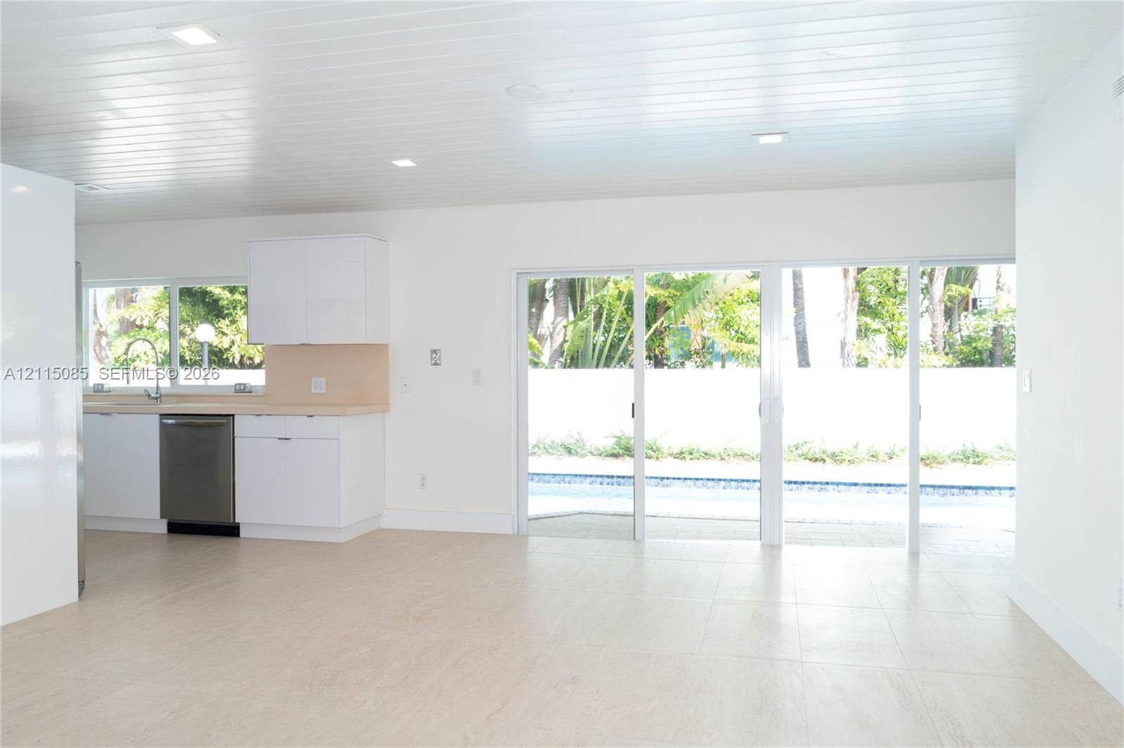 663 Woodcrest Road, Key Biscayne, Key Biscayne, FL 33149 Kitchen featuring white cabinetry, light-toned countertops, and stainless steel dishwasher, with light-toned porcelain tile flooring and sliding glass doors opening to a swimming pool