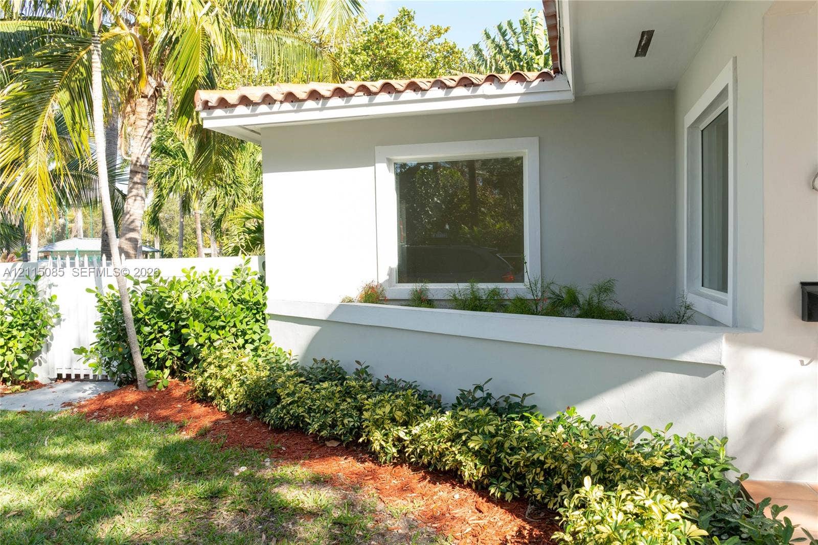 663 Woodcrest Road, Key Biscayne, Key Biscayne, FL 33149 Exterior featuring light-toned stucco siding, a terracotta tile roofline, crisp white window trim, and a manicured foundation garden with mulch beds