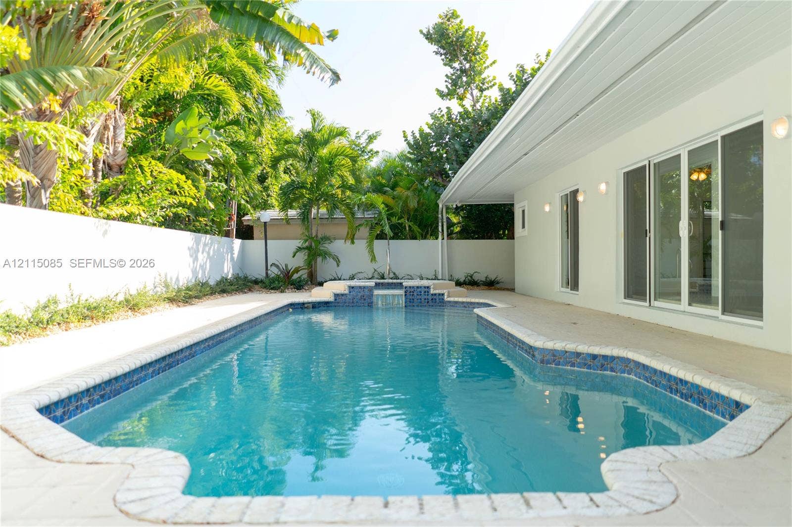 663 Woodcrest Road, Key Biscayne, Key Biscayne, FL 33149 In-ground swimming pool featuring a tiled waterfall element, stone-paver decking, and a perimeter privacy wall