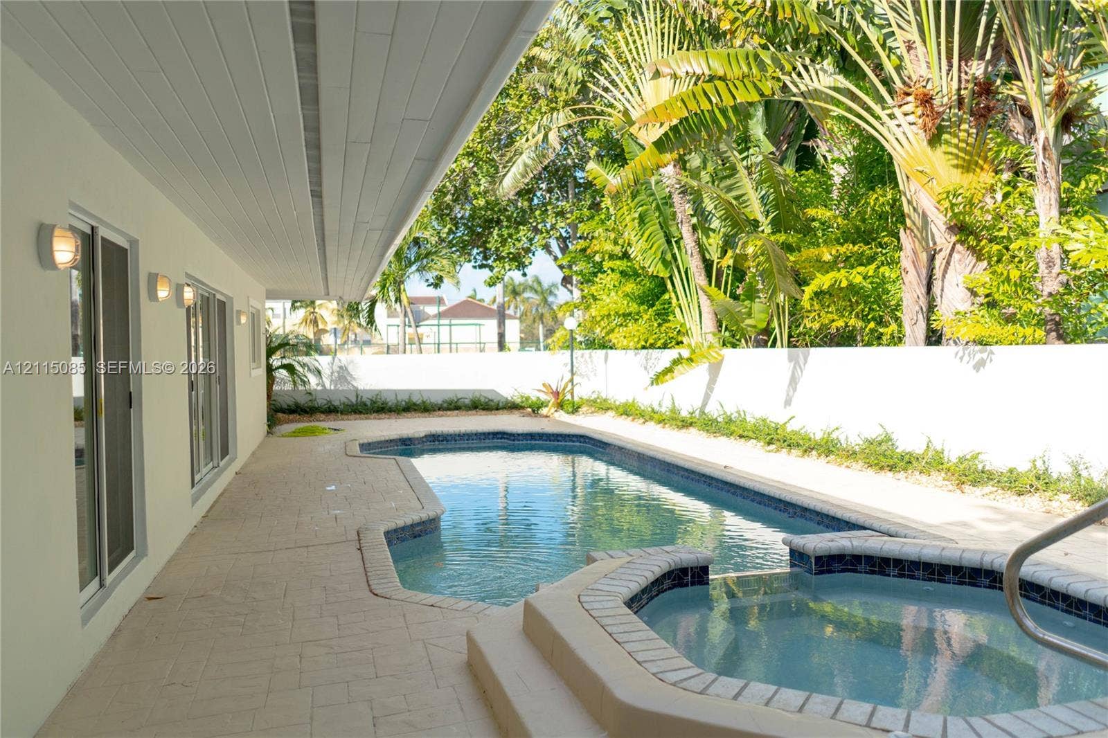 663 Woodcrest Road, Key Biscayne, Key Biscayne, FL 33149 Covered patio featuring stone-tiled flooring, swimming pool with tiled coping, integrated spa, and surrounding privacy wall