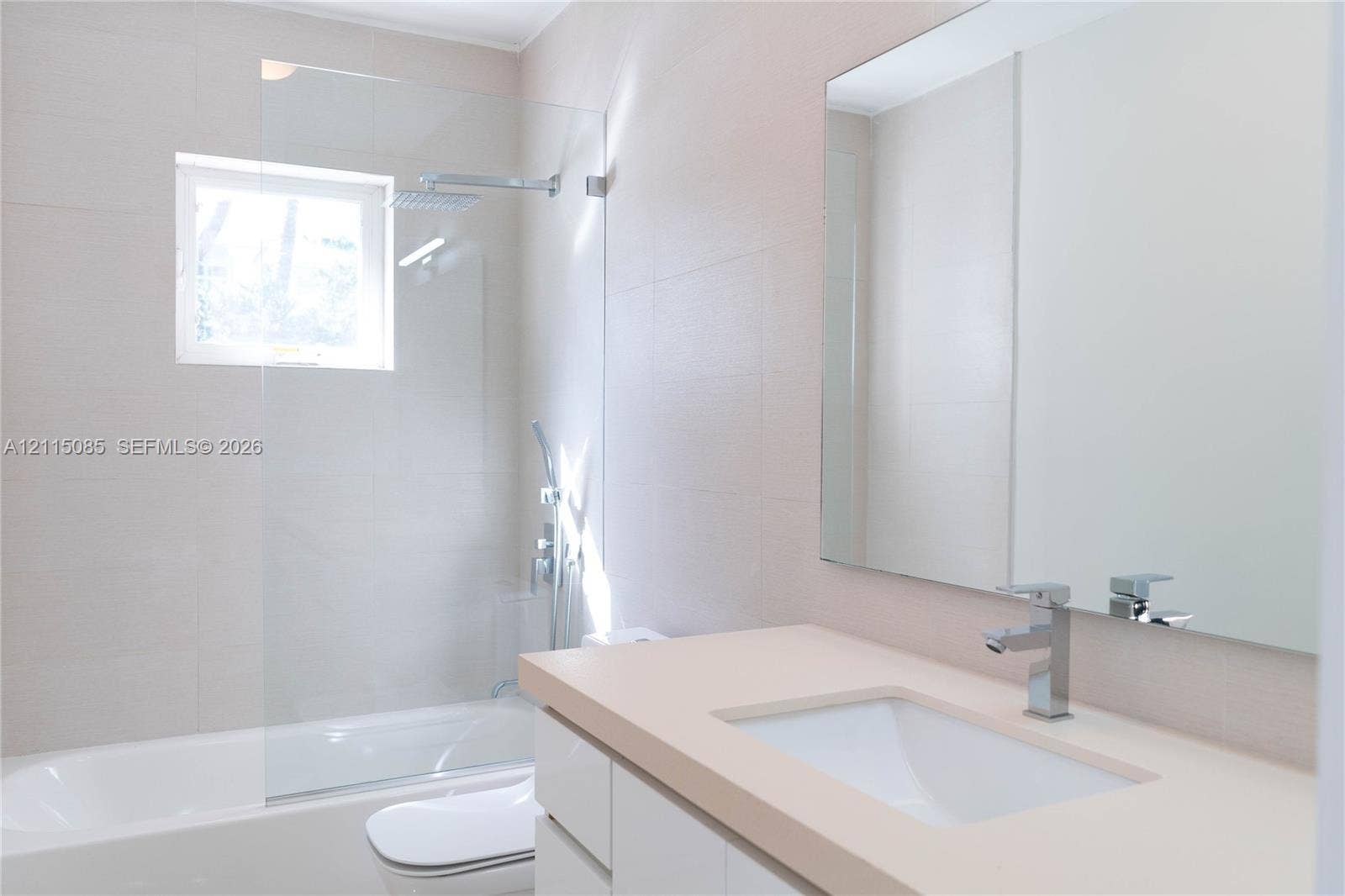 663 Woodcrest Road, Key Biscayne, Key Biscayne, FL 33149 Bathroom featuring a white vanity with a solid surface countertop, an undermount sink, a frameless glass shower partition, wall-mounted shower hardware, and a large plate glass mirror