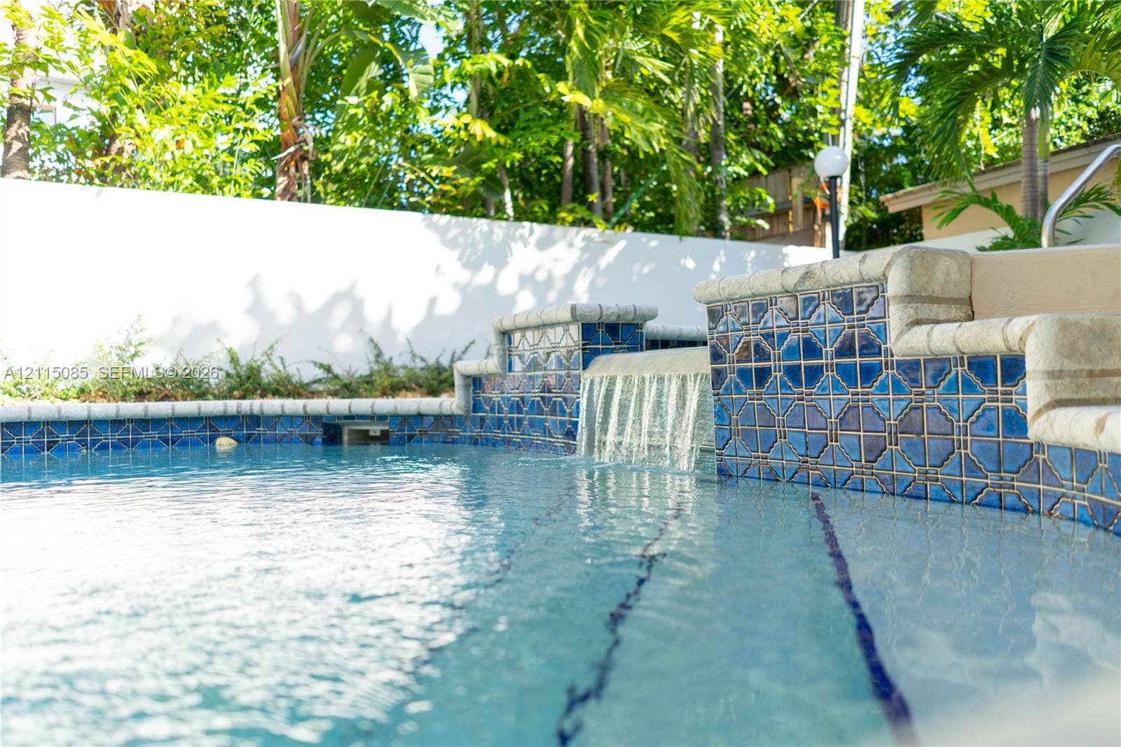 663 Woodcrest Road, Key Biscayne, Key Biscayne, FL 33149 Swimming pool featuring decorative blue tiled accents, a built-in water feature, tiered pool steps, and a solid perimeter privacy wall