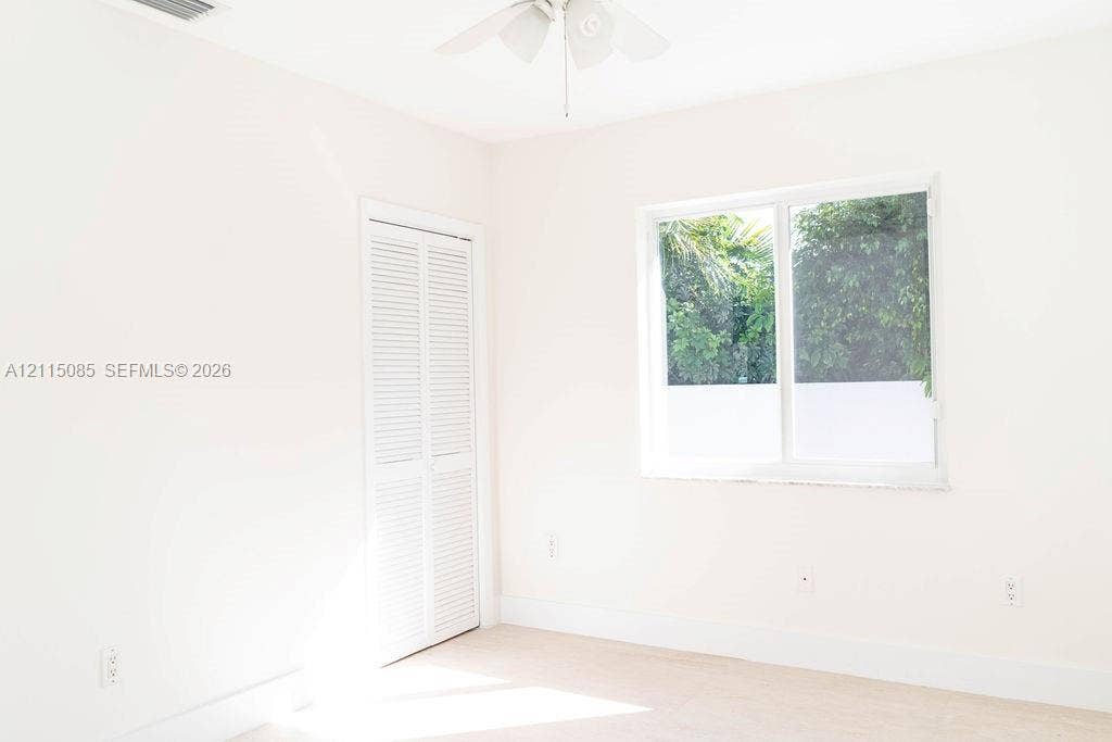 663 Woodcrest Road, Key Biscayne, Key Biscayne, FL 33149 Neutral-toned room featuring a white dual-pane sliding window, closet with white louvered doors, and a ceiling-mounted fan
