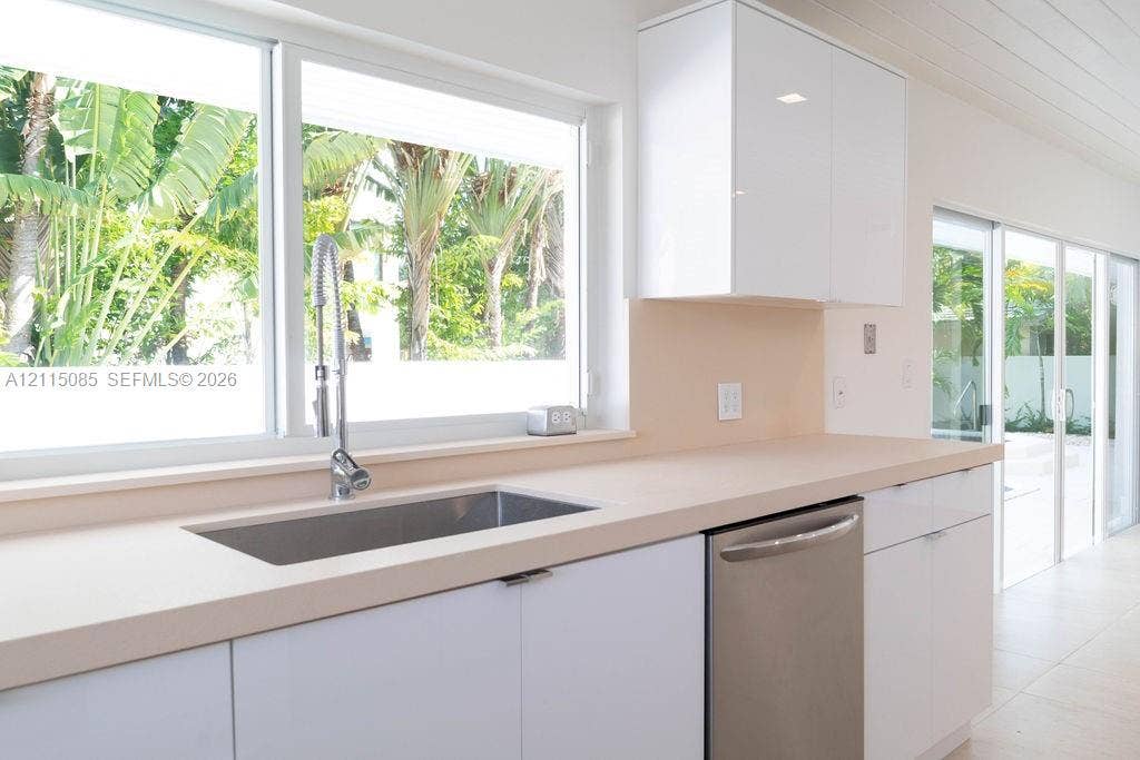 663 Woodcrest Road, Key Biscayne, Key Biscayne, FL 33149 Kitchen featuring white high-gloss cabinetry, stone-surface countertops, a stainless steel undermount sink with a gooseneck faucet, integrated stainless steel dishwasher, and sliding glass doors
