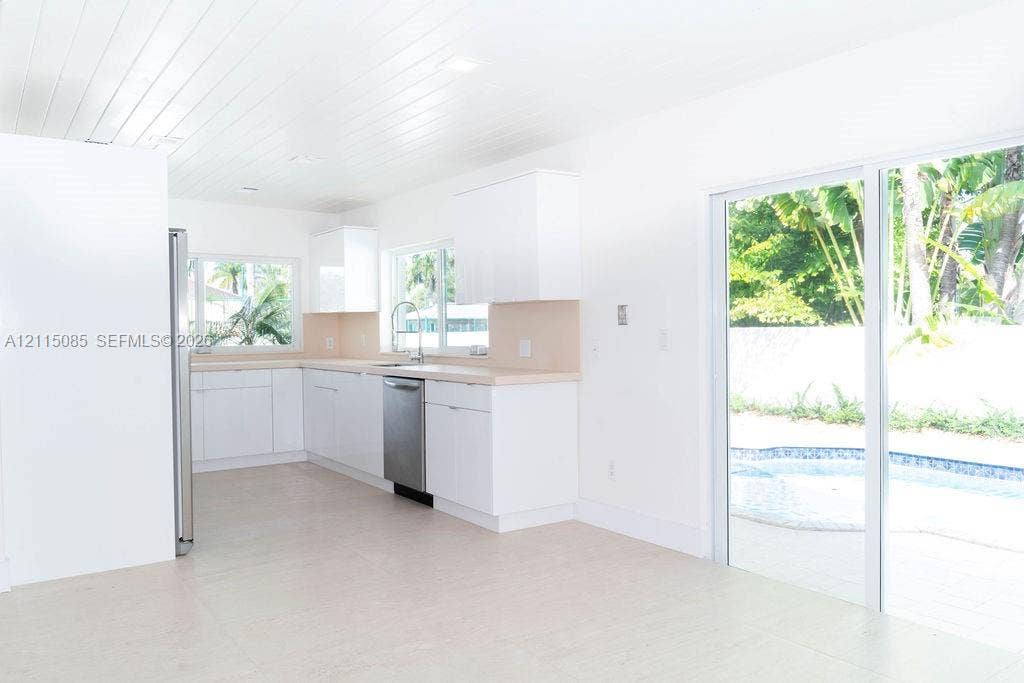 663 Woodcrest Road, Key Biscayne, Key Biscayne, FL 33149 Kitchen featuring white cabinetry, solid-surface countertops, stainless steel dishwasher, tongue-and-groove plank ceiling, and sliding glass doors