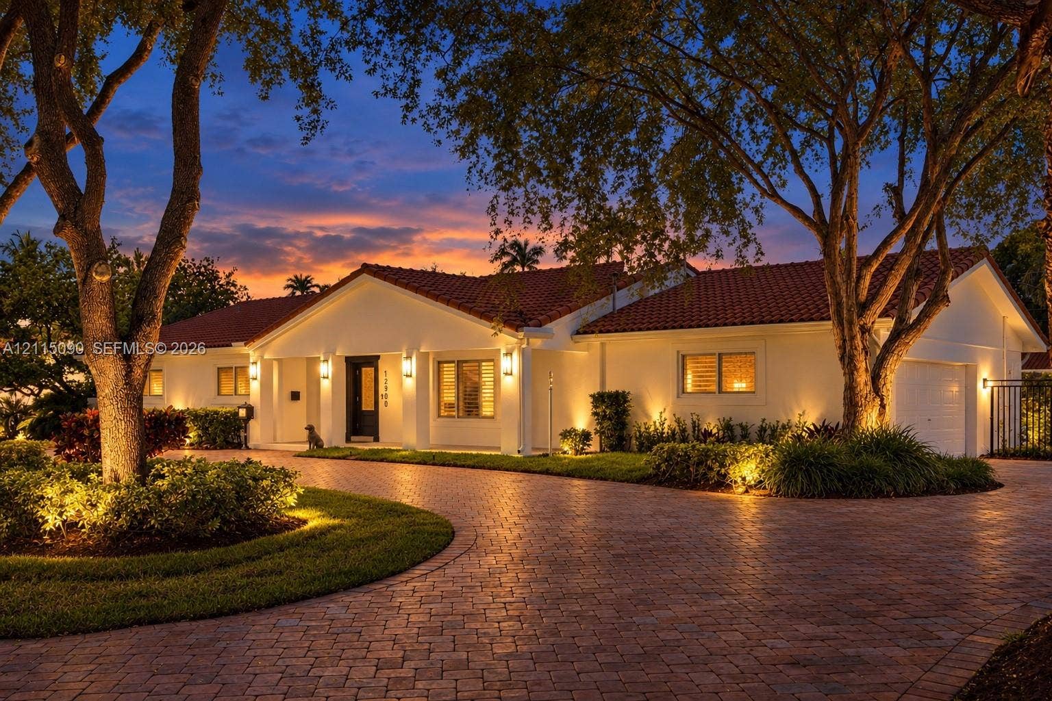 12900 SW 71st Avenue, Pinecrest, Pinecrest, FL 33156 Single-story residence featuring a tile roof, light-toned exterior finish, and a brick-paver circular driveway surrounded by mature landscaping