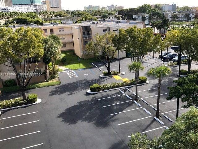 7715 SW 86th Street, #A2-402, Miami, Miami, FL 33143 Asphalt parking lot featuring designated stall markings, mature trees, landscaped shrubbery, and pole-mounted exterior lighting