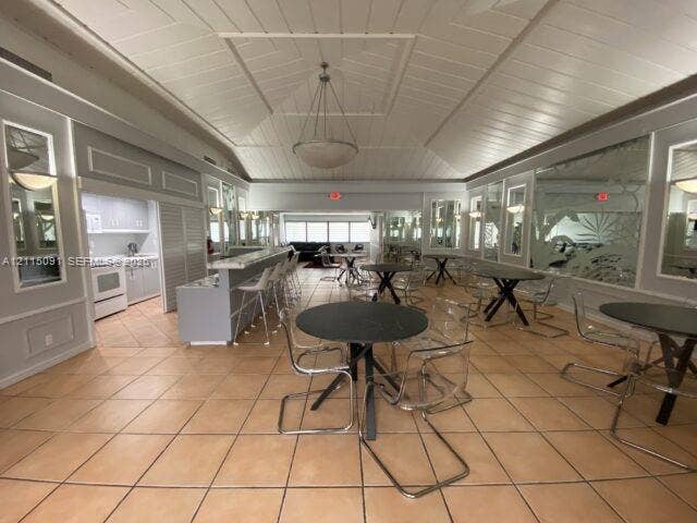 7715 SW 86th Street, #A2-402, Miami, Miami, FL 33143 Vaulted ceiling with shiplap-style paneling, ceramic tile flooring, built-in bar with stone countertop, and decorative wall paneling with inset mirrors
