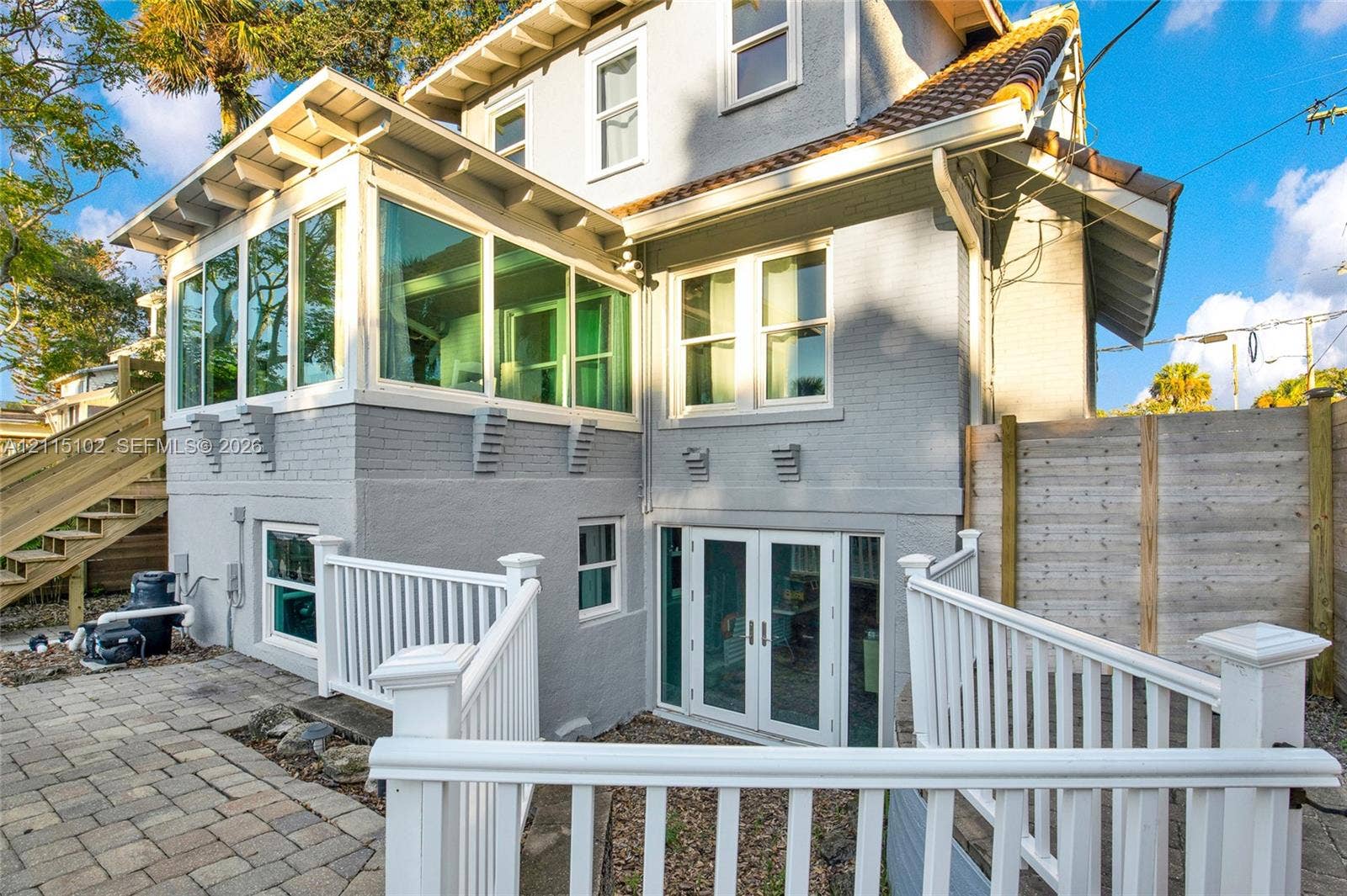 110 S Peninsula, New Smyrna Beach, FL 32169 Painted brick exterior featuring an expansive sunroom with wrap-around windows, paved patio, double-door glass entrance, and white railing enclosures
