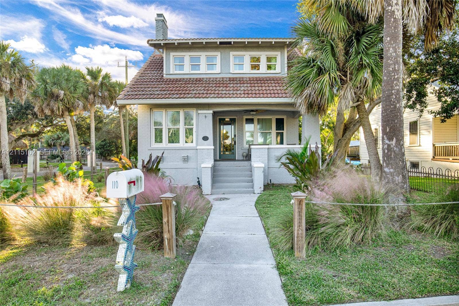 110 S Peninsula, New Smyrna Beach, FL 32169 Craftsman-style exterior featuring a tile roof, covered front porch with concrete stairs, masonry chimney, and multi-pane windows
