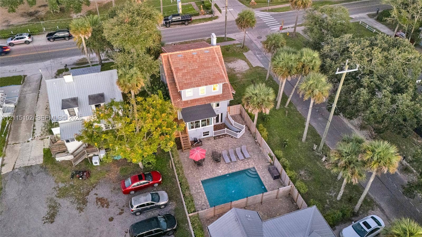 110 S Peninsula, New Smyrna Beach, FL 32169 Aerial view featuring a multi-story residence with a red-toned roof, an in-ground swimming pool, a stone-paver patio, and mature palm trees