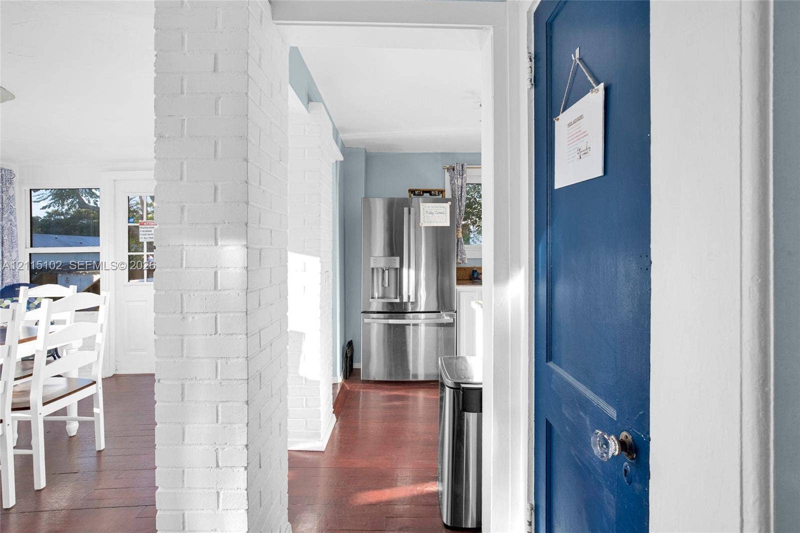 110 S Peninsula, New Smyrna Beach, FL 32169 Interior space featuring a white-painted brick structural column, wood-finish flooring, and a blue-painted solid wood door with a glass knob
