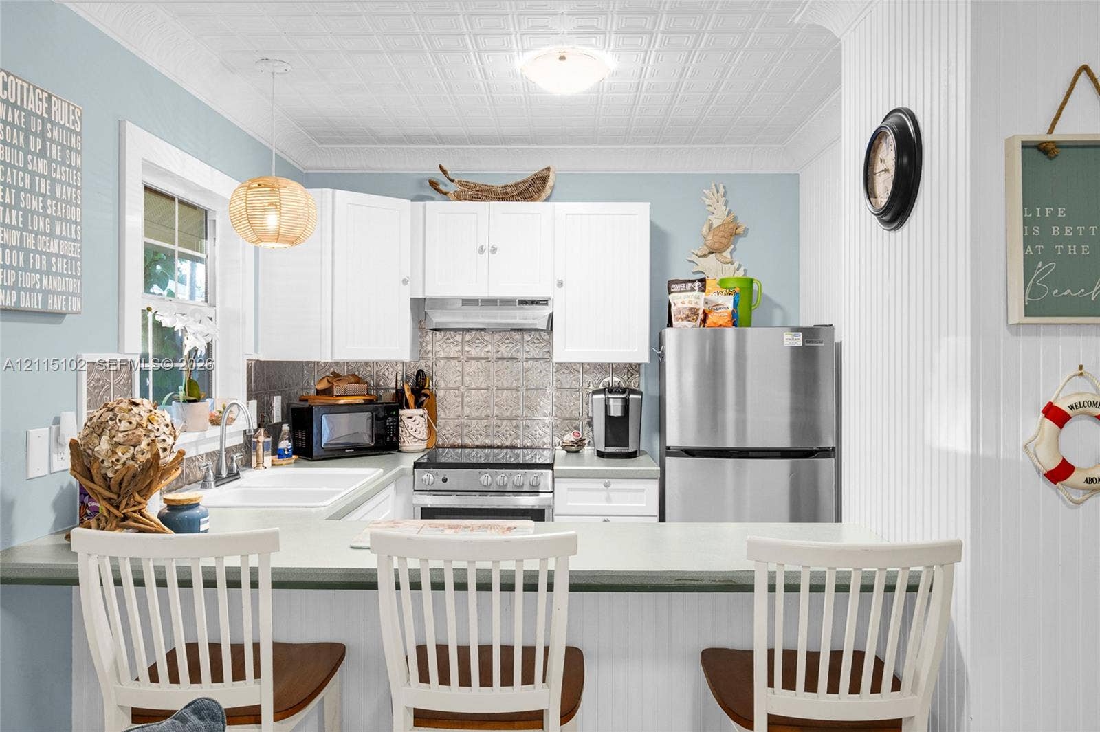 110 S Peninsula, New Smyrna Beach, FL 32169 Kitchen featuring white cabinetry, metallic patterned backsplash, white farmhouse-style dual-basin sink, beadboard wall paneling, and a decorative pressed-tin style ceiling